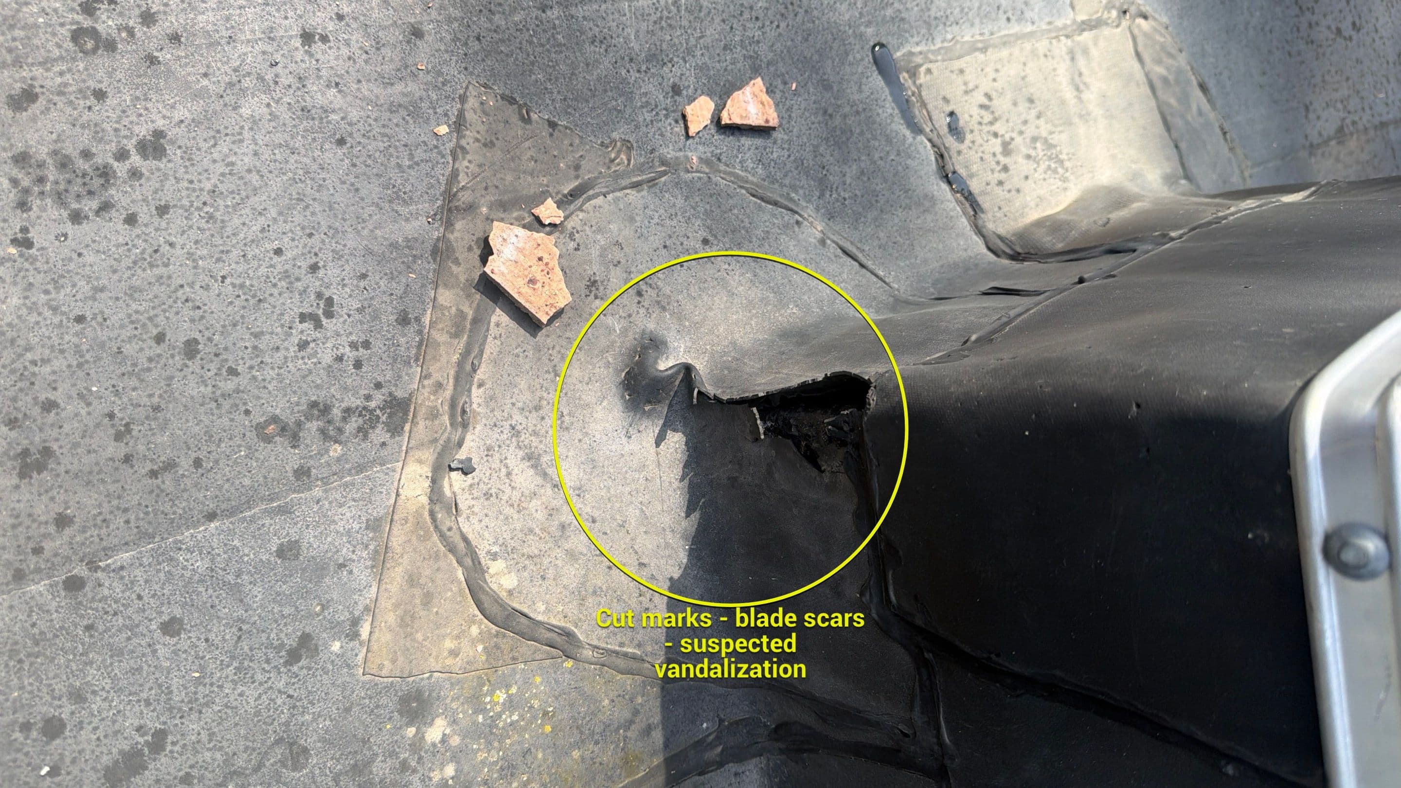Clean blade-like cut marks in the EPDM membrane near the chimney curb — damage that does not come from hail; suspected vandalism